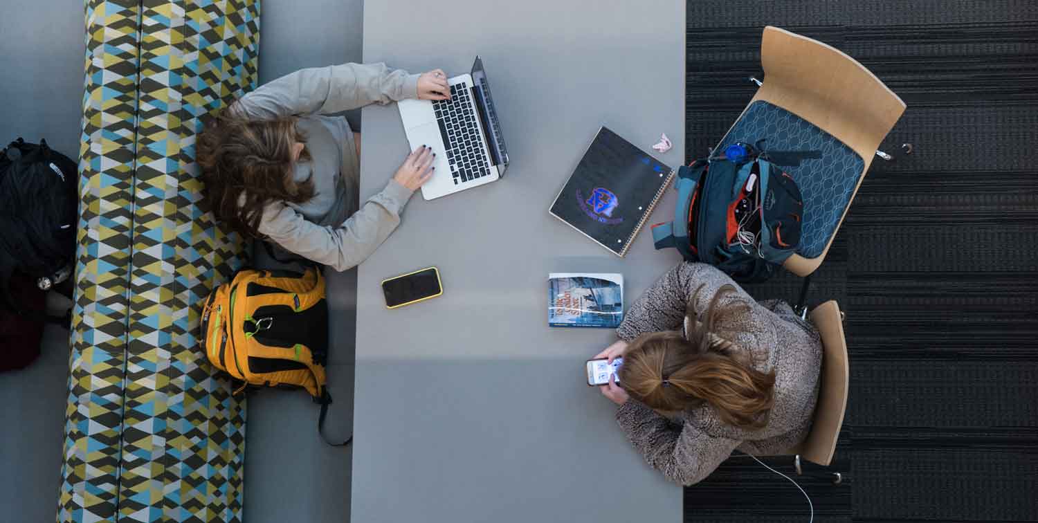 Students using electronic devices at a table on campus