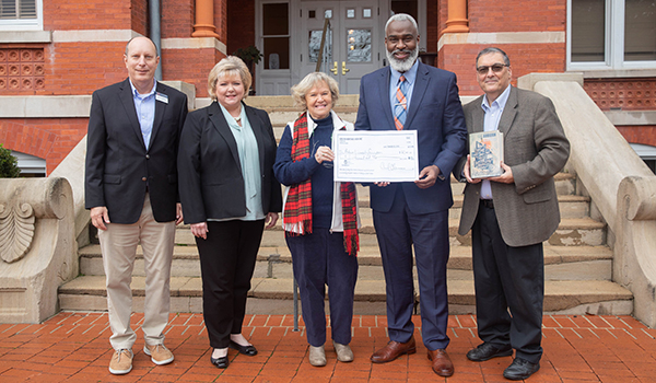 Five people stand in front of Samford Hall during a check presentation for a book called 'Street Names'