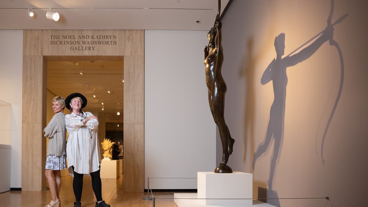 two people standing back to back smiling in front of a sculpture