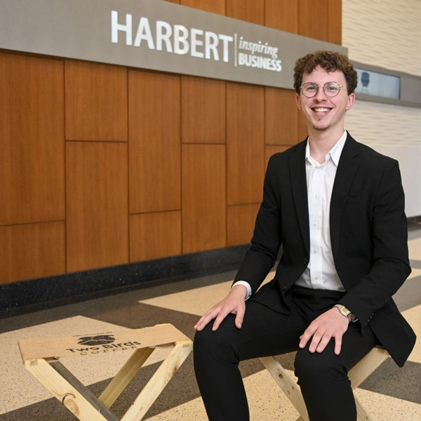 student smiling sitting in front of Harbert sign