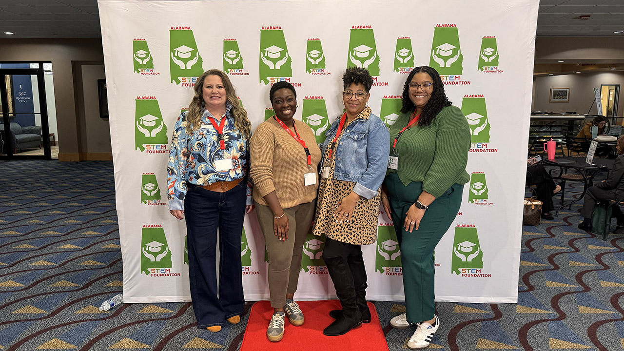 Four GEAR UP Achieve staff members pose for a photo in front of a backdrop at the Alabama STEM Education and Workforce conference.