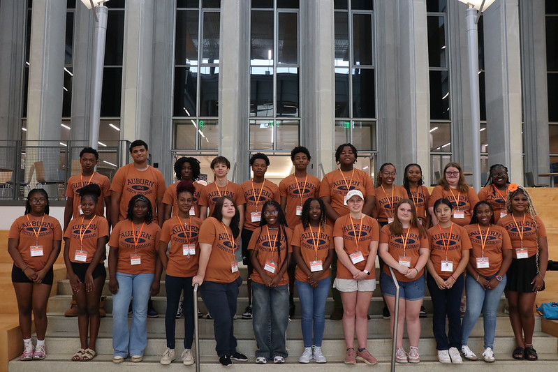 Two rows of GEAR UP Achieve students in matching orange Auburn University shirts pose for a photo on a staircase.