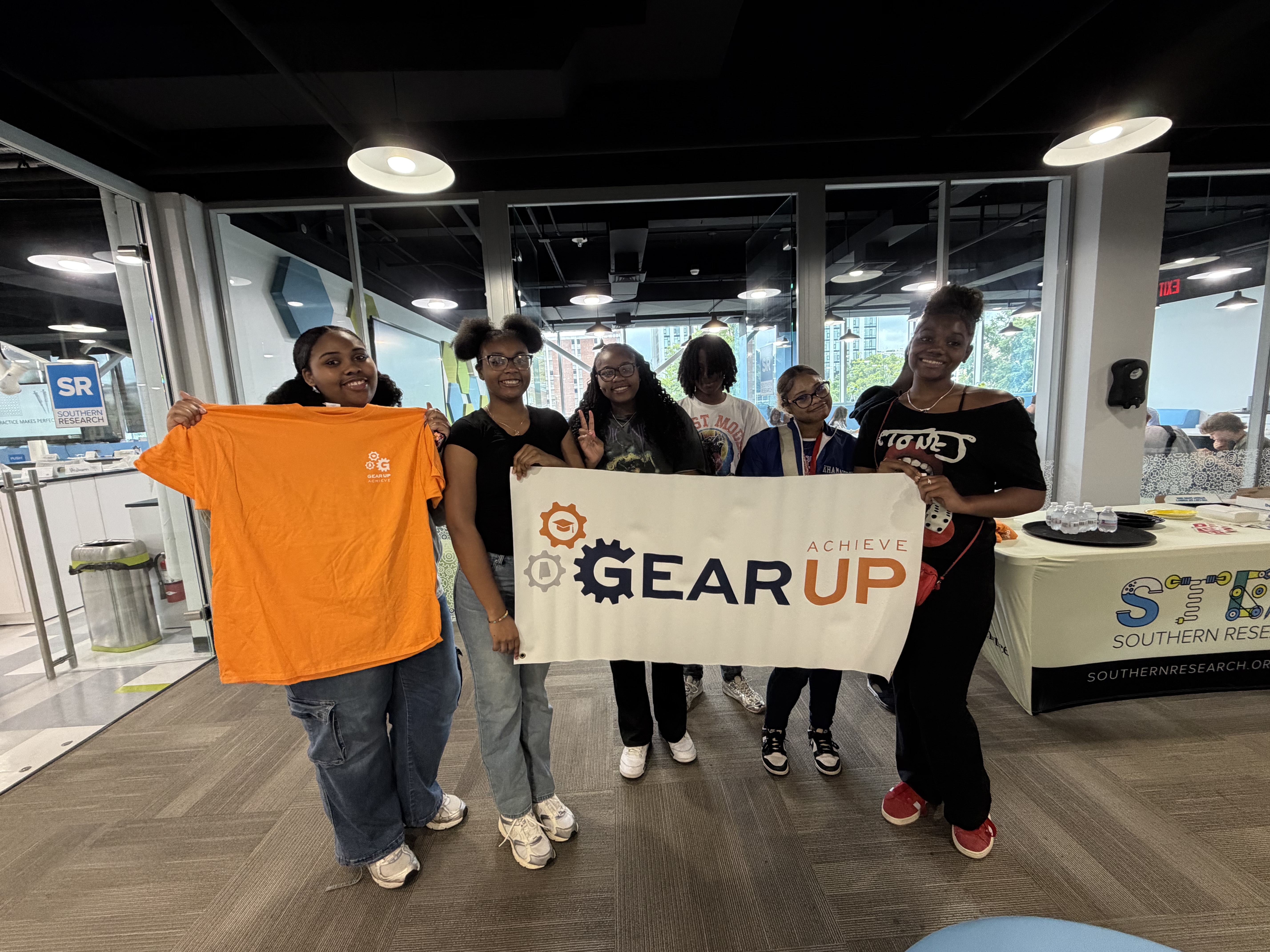 A group of six GEAR UP Achieve students pose for a photo holding a GEAR UP Achieve logo banner.