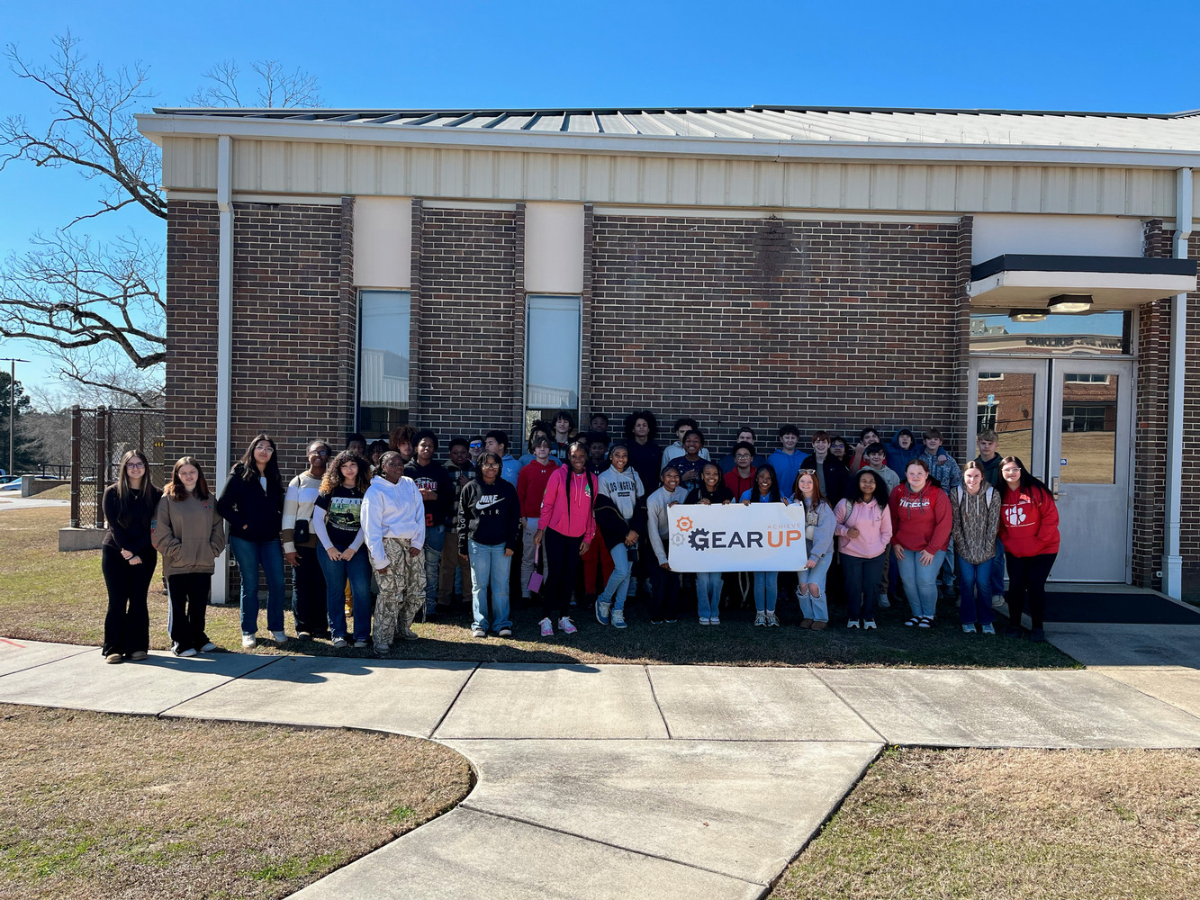A group of GEAR UP Achieve students pose with a GEAR UP Achieve logo banner.