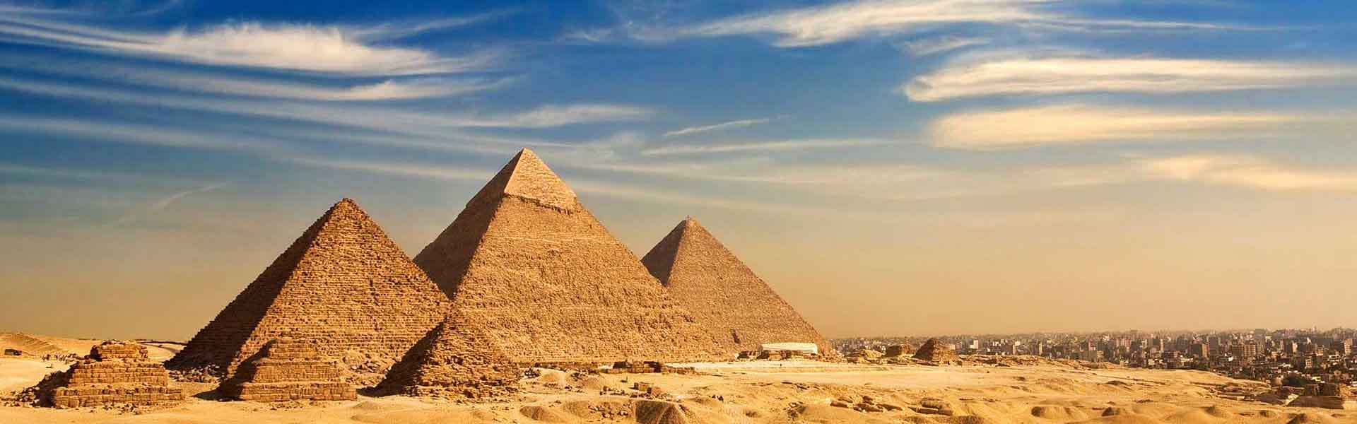 Three pyramids at Giza in Egypt rising from the desert under a partly clouded sky.