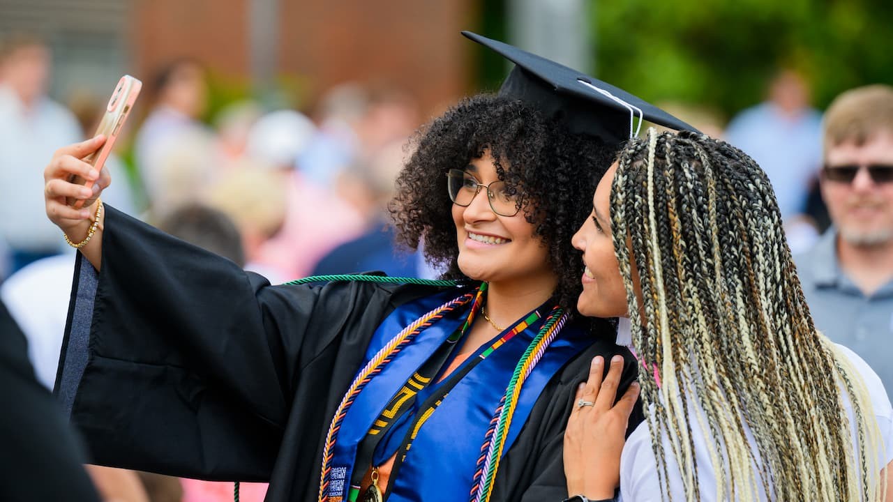 two students taking a selfie, one in a cap and gown