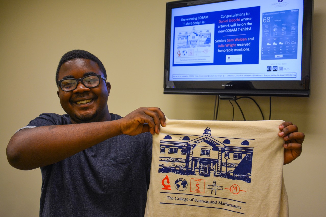 Daniel Udochi holds up his winning artwork design on the new COSAM T-shirt. 