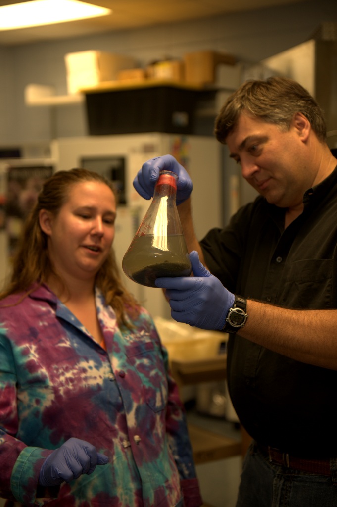 Ken Halanych holds and examines sediment in a large flask while student looks on