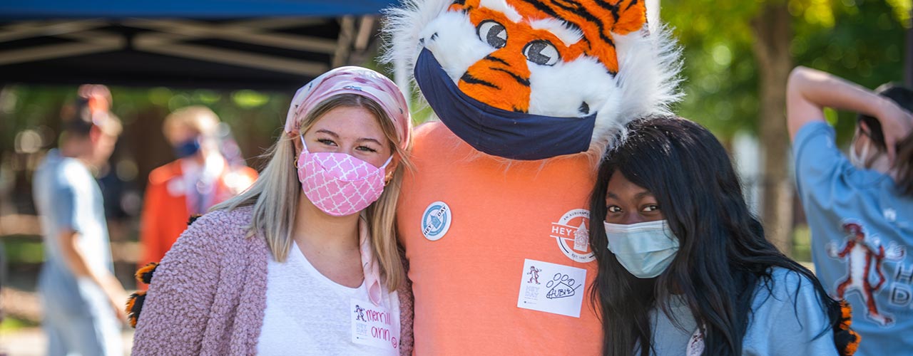 Two students in masks pose with Aubie.