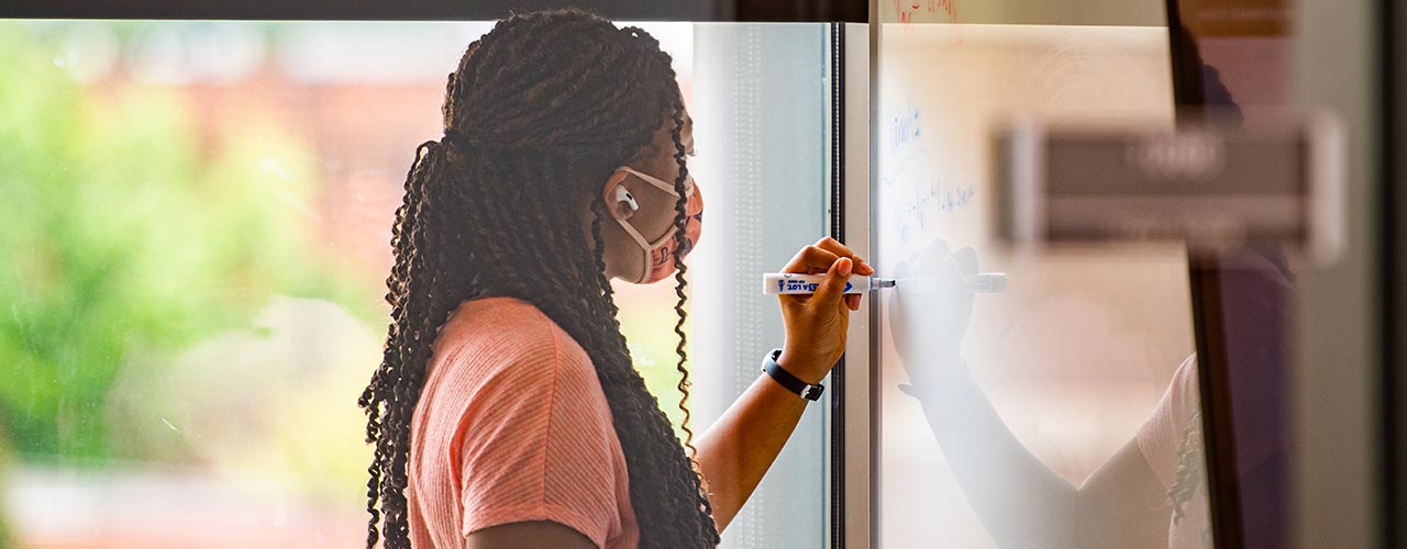 A student writes on a whiteboard.