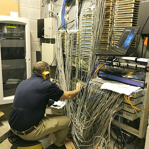 A member of the telecommunications team adjusting switches in a storage closet