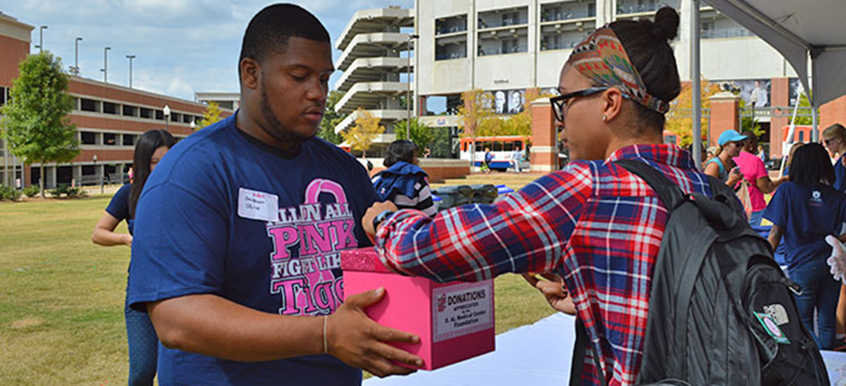 Male college student holds donation box while female student puts money in it at All in All pink event