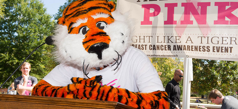 Auburn mascot, Aubie, stands at podium with all in all pink banner behind him