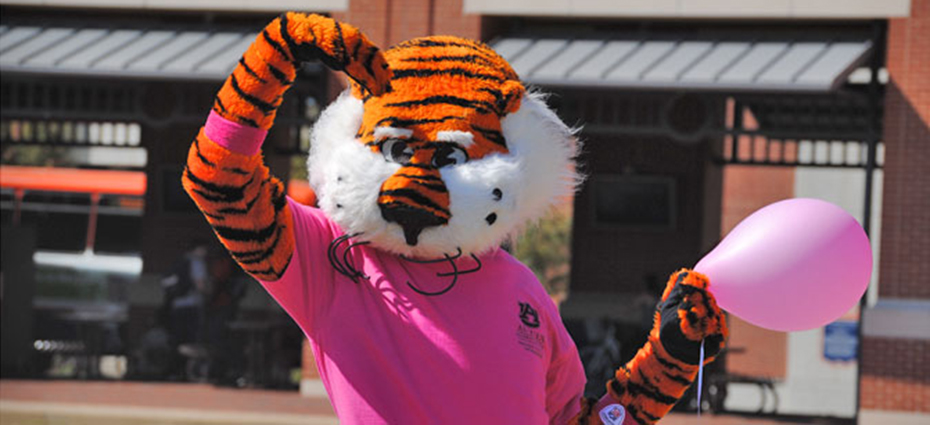 Auburn mascot, Aubie, give a salute while wearing a pink shirt and holding a pink balloon