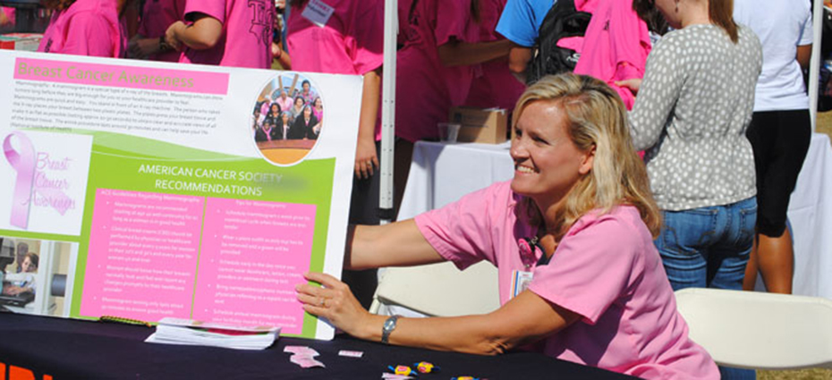 Woman wearing pink scrubs holds american cancer society poster at all in all pink event