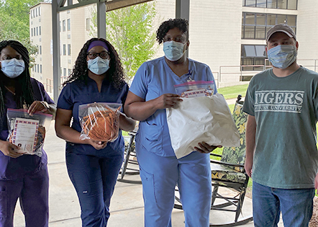 Three women wearing scrubs and holding bags of face masks and man in green Auburn shirt stand outside of building.