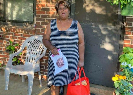 Woman stands on porch holding donation bag and mask from Church of Highlands outreach