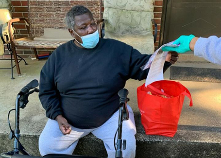 Man sits in chair reaching for donated mask from Church of Highlands outreach volunteer