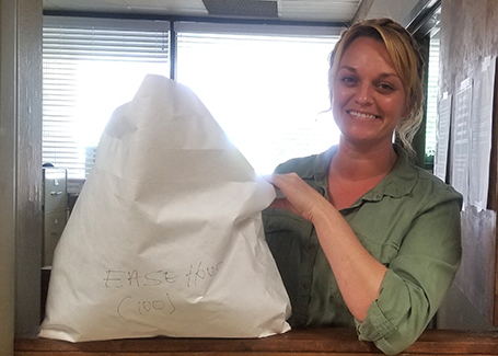 Blonde woman wearing green shirt holds up large envelope of donated face masks.