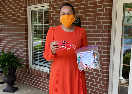 Woman in red dress wearing face mask holds up colorful face masks that have been donated.