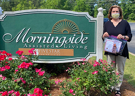 Woman holding envelope of face masks next to Morningside Assisted Living sign.