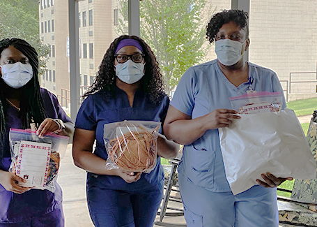 Three women wearing scrubs and holding bags of face masks standing outside of building.