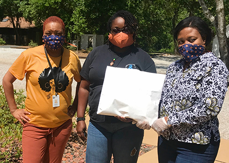 Three women stand outside with bag of face masks that were donated.