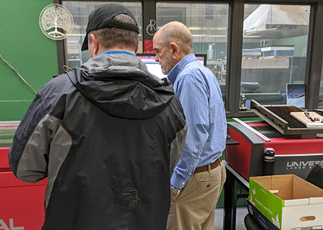 Two men standing next to laser cutting machine.