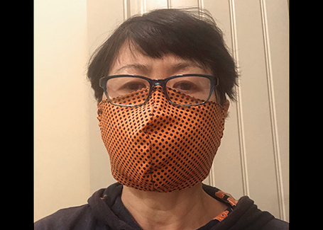 Asian man with glasses wears orange fabric face mask that he sewed.