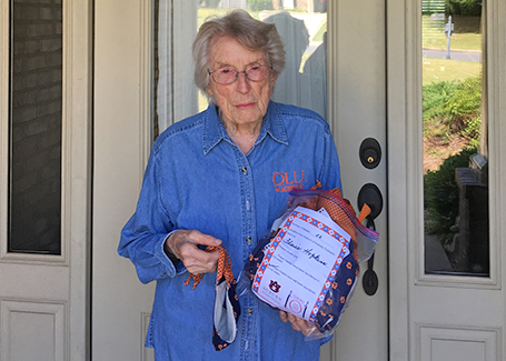 Older woman wearing glasses stands in front of door holding masks that she's sewn.