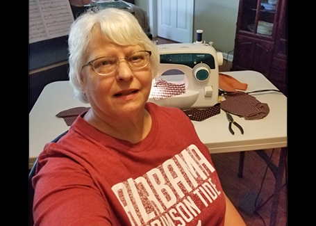 Woman sits in front of sewing machine wearing maroon Alabama Crimson tide shirt