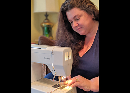 Woman sits at sewing machine making orange and blue face masks