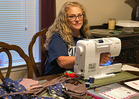 Woman sitting at a sewing machine with fabric pieces on the table in front of her.