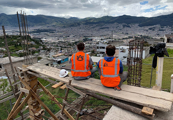 Two students sitting on building scaffolding looking out over city.