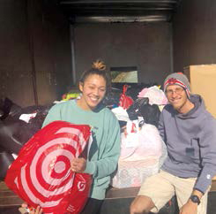 Two people sit in back of truck with bag of christmas donations