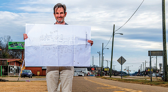Man holds up blueprint in front of road