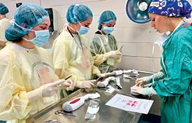 Young adults wearing masks, gowns and hairnets prepare for mock surgery during summer camp