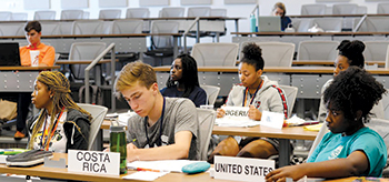 Students sit at tables with country markers in front of them during world affairs camp