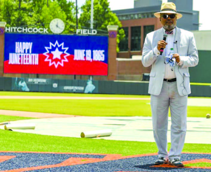 Man in suit holds microphone standing in middle of baseball field