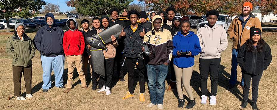 A group of male and female students stand with drones outside in a field