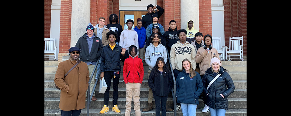 A group of male and female students stand in front of a large building entryway for a tour