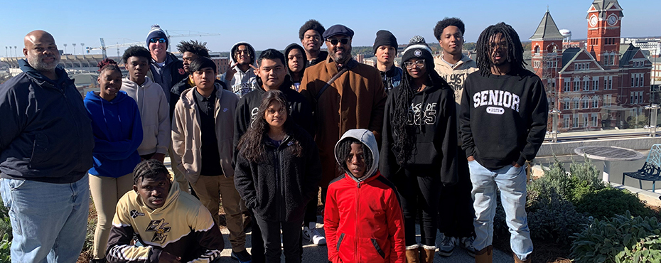 A group of male and female students stand for a picture with a campus backdrop