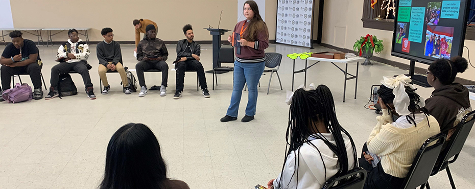 A female guest speaker presents to a group of students in a school auditorium