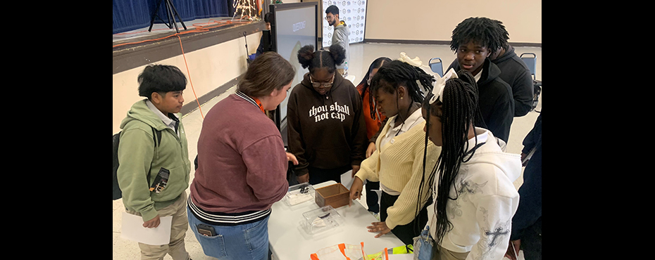 A small group of students observe an insect collection display with a female guest speaker explaining