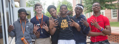 Six young adults hold up to 4 fingers to the camera in front of AU football stadium. 