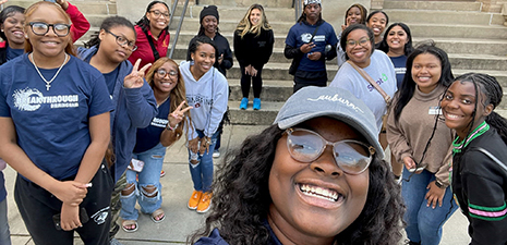 Group of college aged males and females standing outside a red brick building with white columns taking a selfie