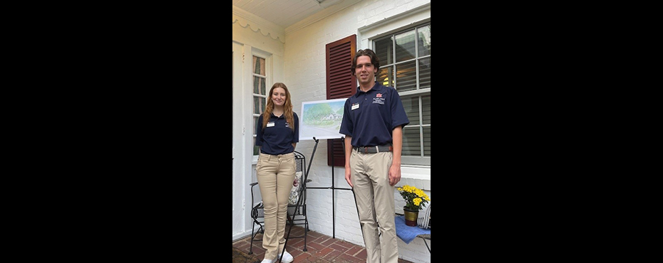 One female and one male student ambassador stand in front of a doorway entry to welcome guests to an event