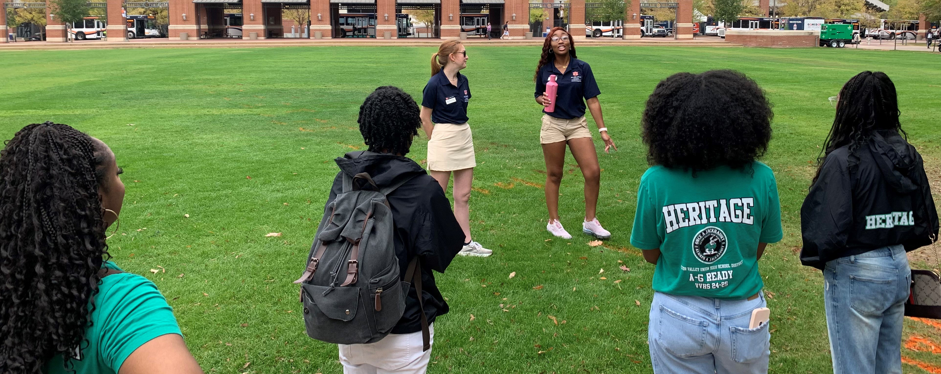 2 female students lead a tour for a group of male and female visiting students and teachers