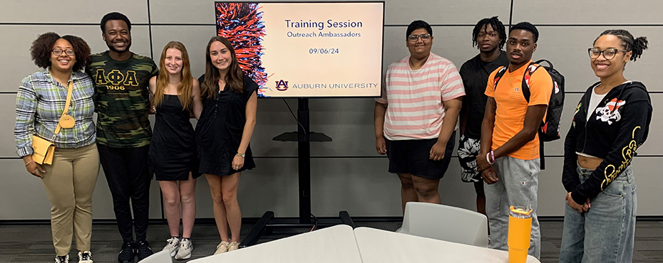    A small group of male and female students smile in front of a smartboard screen after a training.