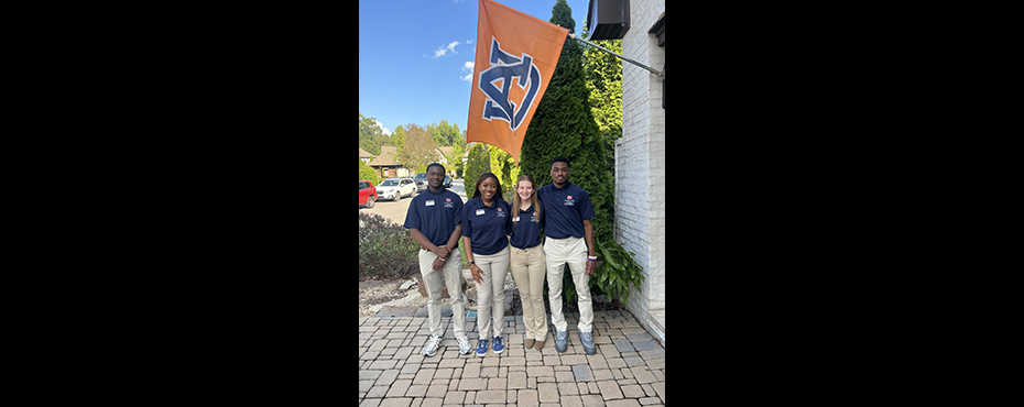 3 female students and 1 male student stand under an Auburn flag for a picture before an event.